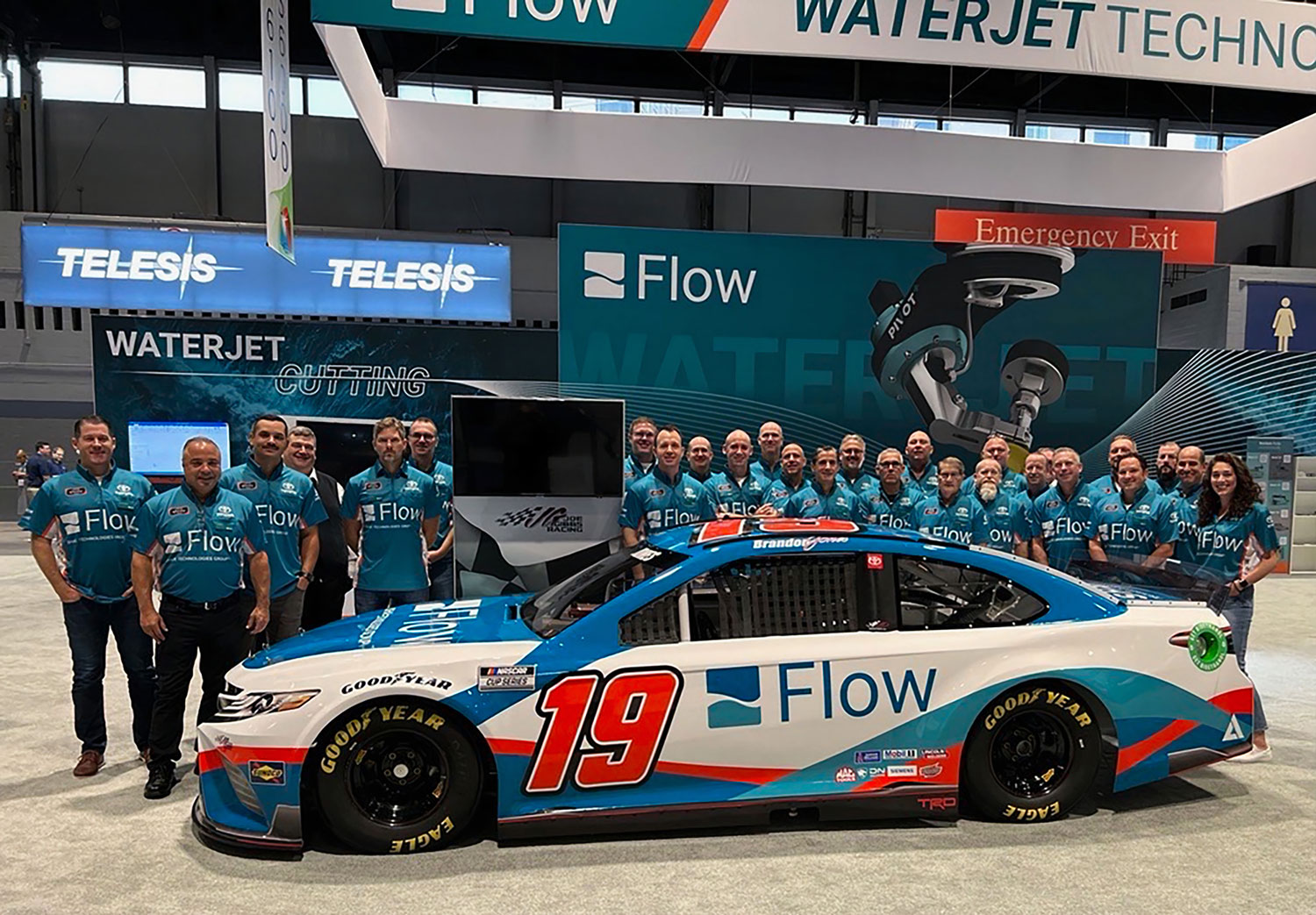 Funcionários da Flow em pé no estande da feira com o #19 Flow Nascar